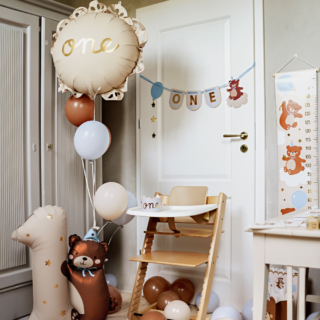 beige folieballon met gouden tekst one en ruches hangt in een tros met bruine en blauwe ballonnen op een kinderkamer met houten, beige en bruine feest versiering