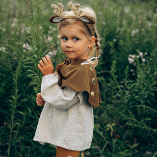 meisje verkleed als hert met een cape, haarband en legging speelt in een grasveld