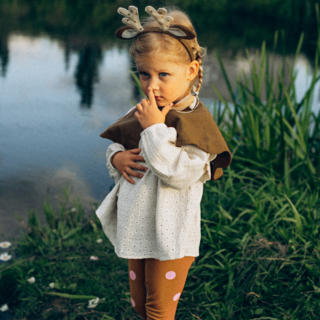 meisje verkleed als hert met een cape, haarband en legging speelt in een grasveld